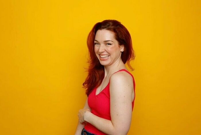 Smiling red-haired woman in a red top posing against a yellow background representing iconic actors who dominated Hollywood.