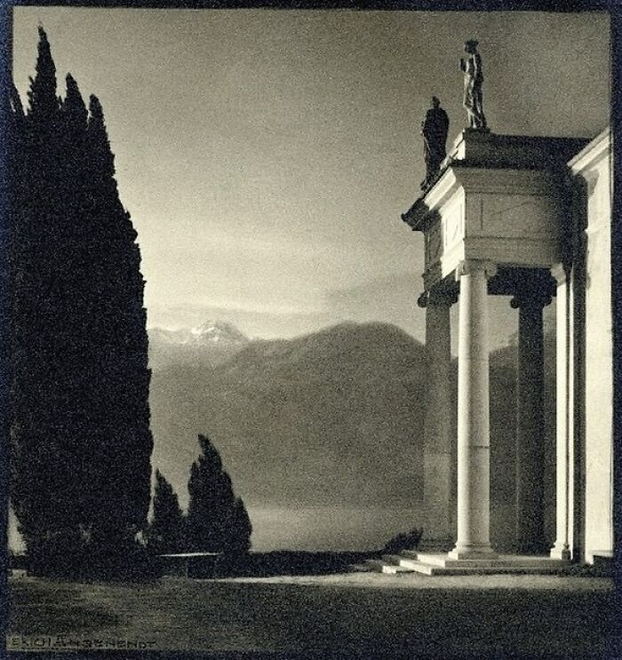 Classical architectural structure with columns and statues overlooking a scenic mountainous landscape at dusk.