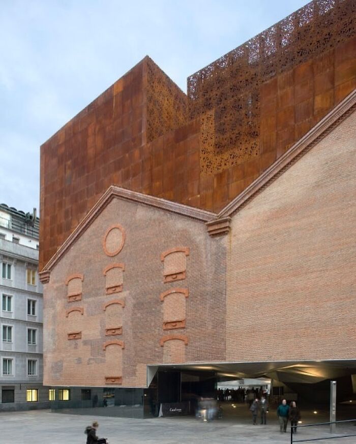 Modern architectural structure blending rusted metal and brick with unique design elements in an urban setting.