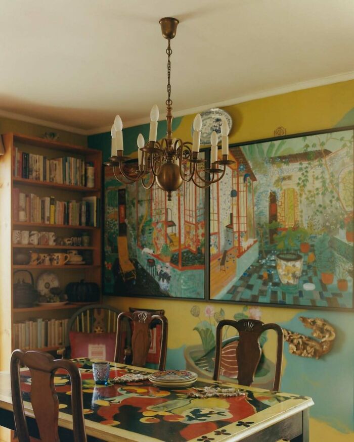 Cozy dining room with bold and beautiful interiors featuring vintage chandelier, colorful table, and artistic wall murals.
