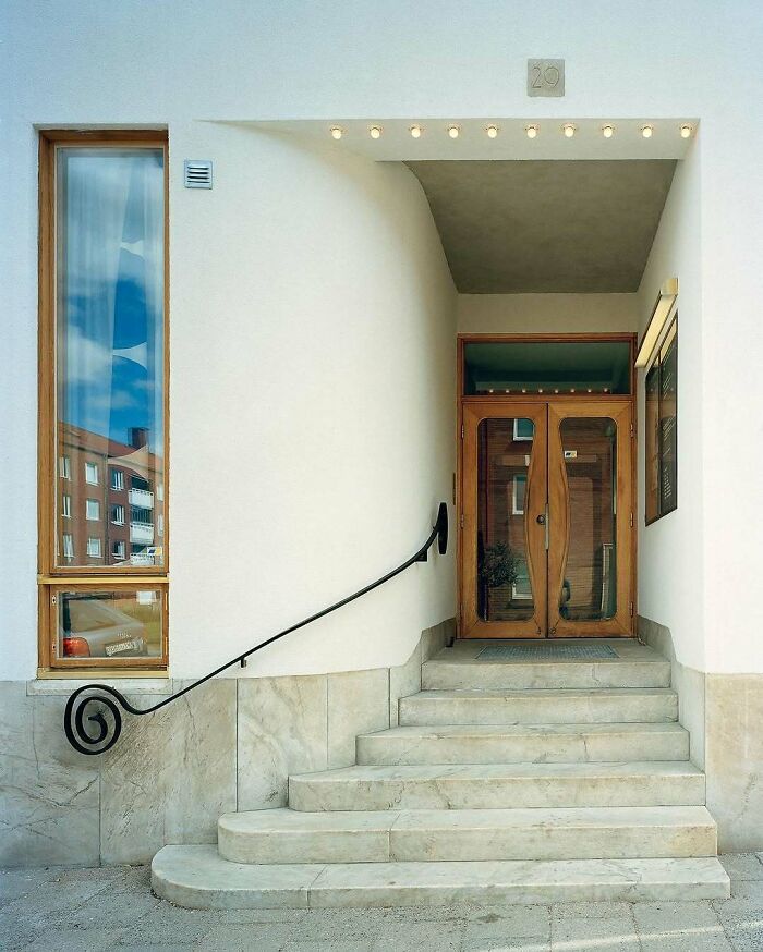 Modern architectural structure featuring unique entrance with curved handrail and wooden framed glass doors.