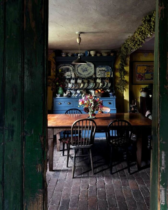Rustic dining room with bold blue cupboard, vintage plates, wooden table, and chairs showcasing beautiful interiors design.