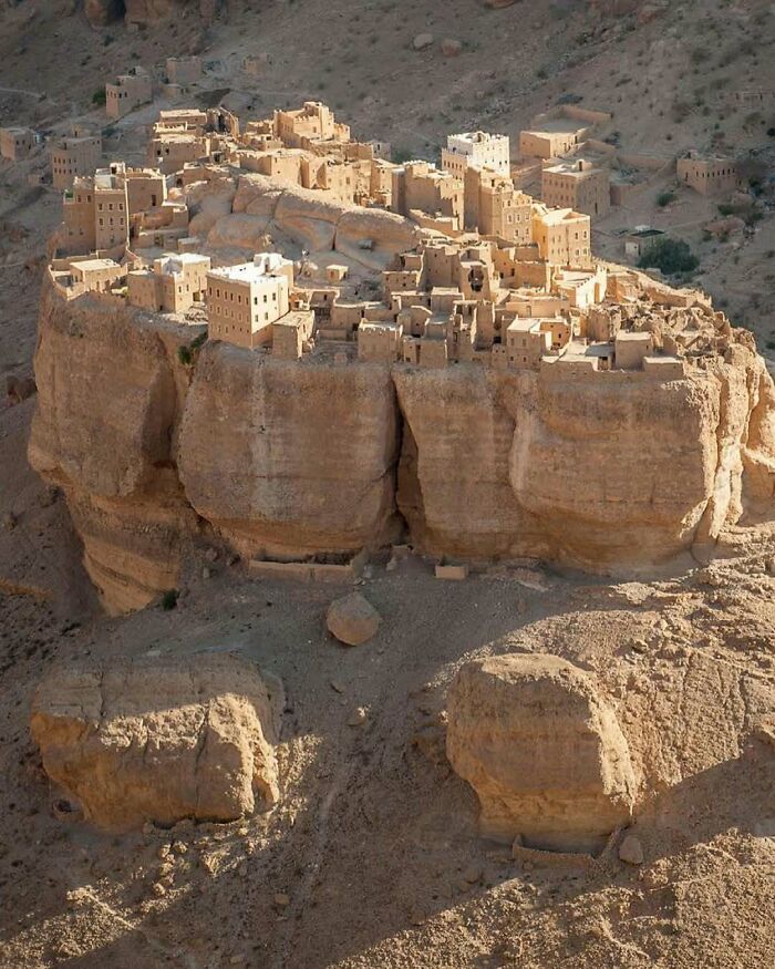 Ancient architectural structures built on a rocky cliff showcasing humanity's creativity and innovative design in a desert landscape.