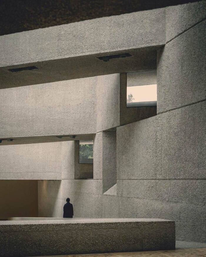 Minimalist concrete architectural structure with geometric shapes and a person standing inside, showcasing creative architectural design.