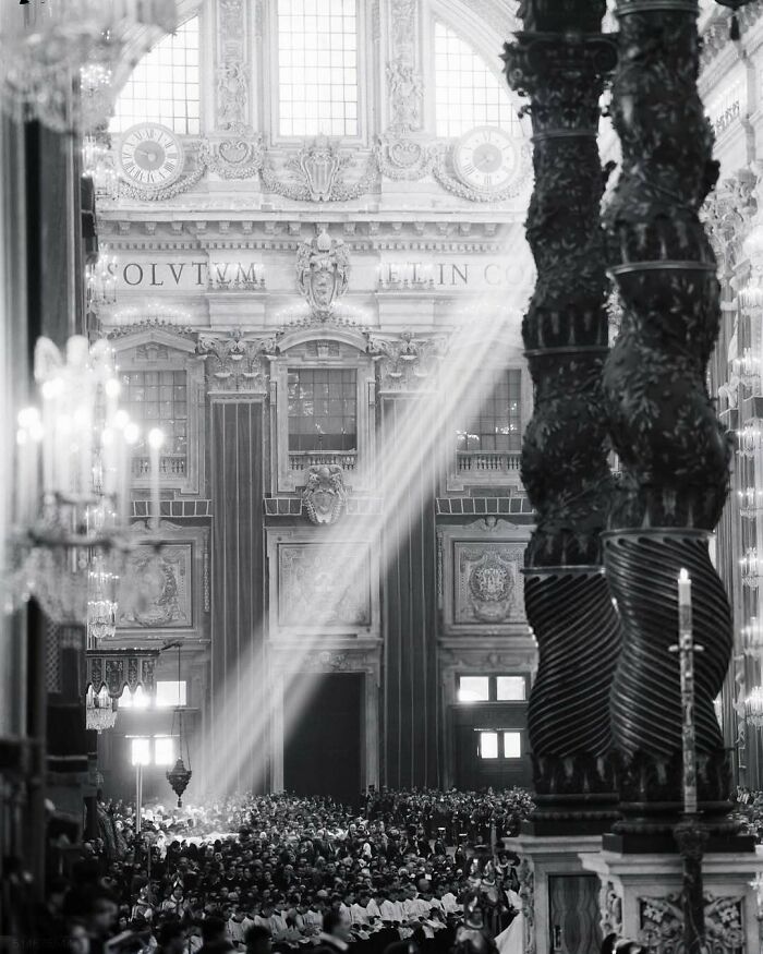 Interior of a grand architectural structure with ornate columns and sunlight streaming through tall windows.