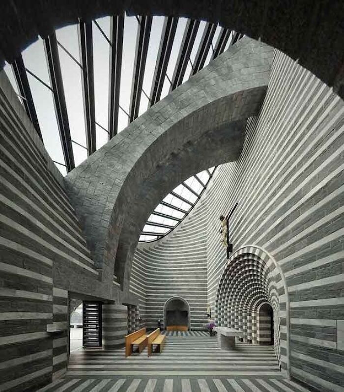 Interior view of a modern architectural structure featuring striped stone walls, arches, and skylights showcasing creativity.