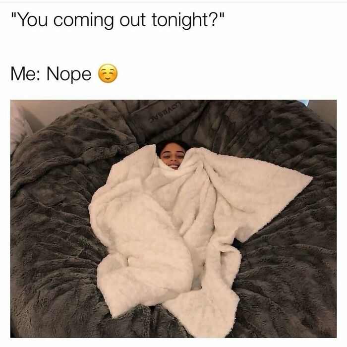 Young woman wrapped in a cozy blanket, smiling and relaxing on a large fluffy couch in a cute wholesome moment.