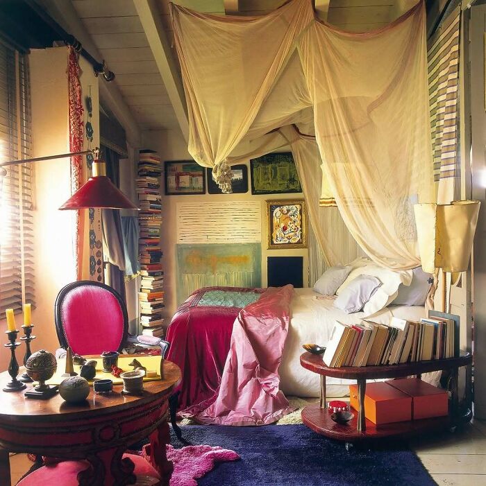 Cozy bold and beautiful interiors featuring a canopy bed, vibrant textiles, stacked books, and eclectic decor elements.