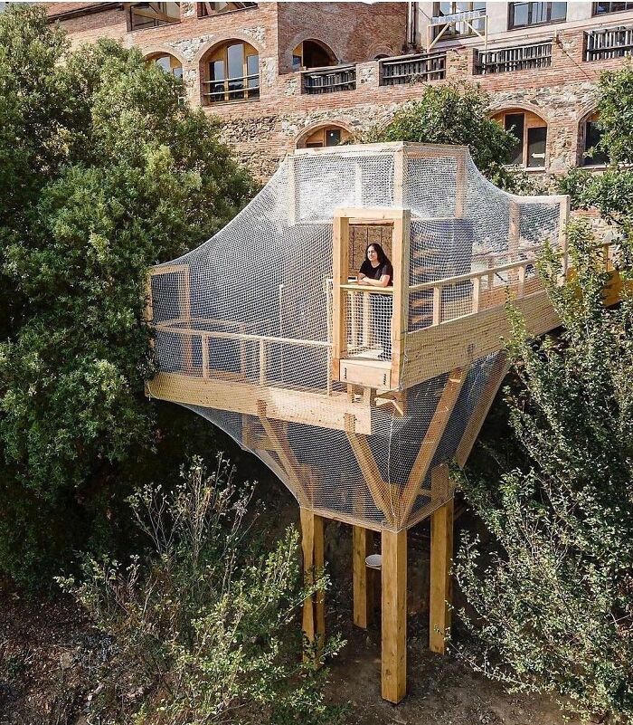 Wooden architectural structure surrounded by greenery with a person standing inside, showcasing amazing creativity in design.