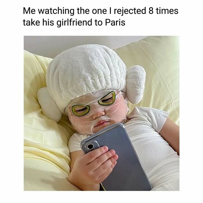 Child in a face mask and towel hat lying on bed, holding a phone, capturing a cute and wholesome moment for girlies.