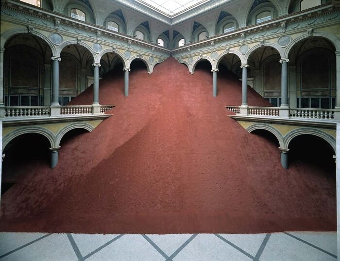 Interior view of an architectural structure featuring large arches and a massive red mound under a glass ceiling.