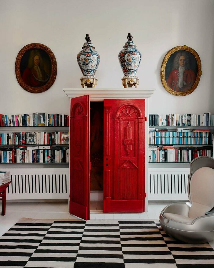 Bold and beautiful interiors featuring a vibrant red cabinet, classic portraits, patterned vases, and a striped rug in a stylish room.