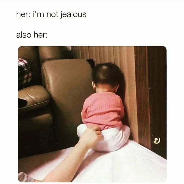 Baby in a pink sweater sitting in a corner with a hand gently poking them, representing cute and wholesome posts for girlies.