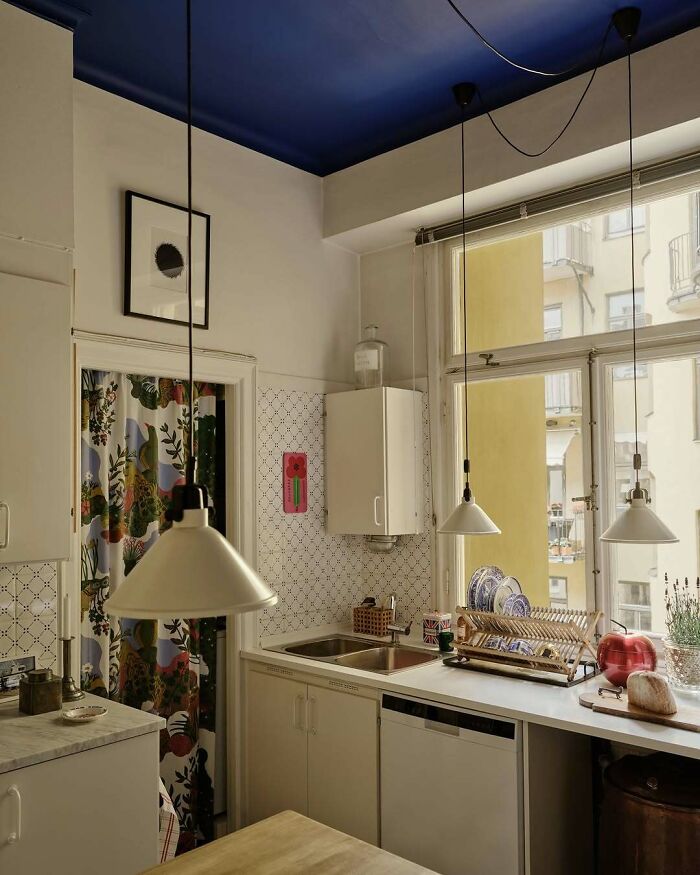Cozy kitchen interior with bold blue ceiling, patterned curtain, and stylish countertop in a beautiful home setting.
