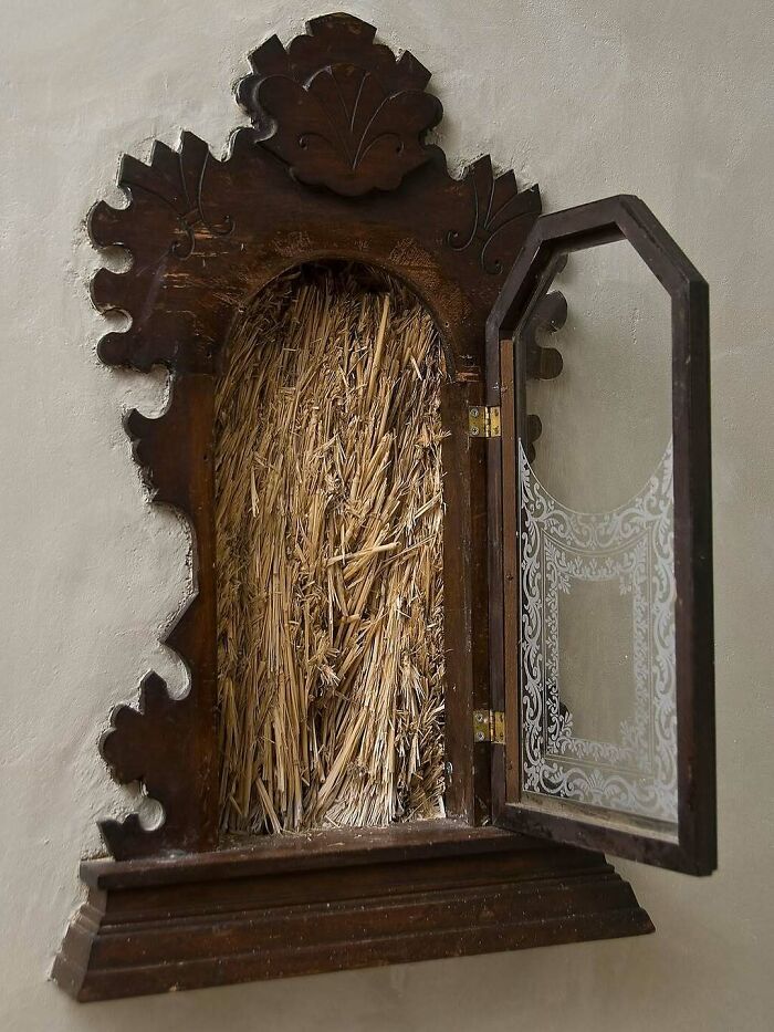 Ornate wooden architectural structure with glass door and intricate carved frame showcasing dried straw interior.