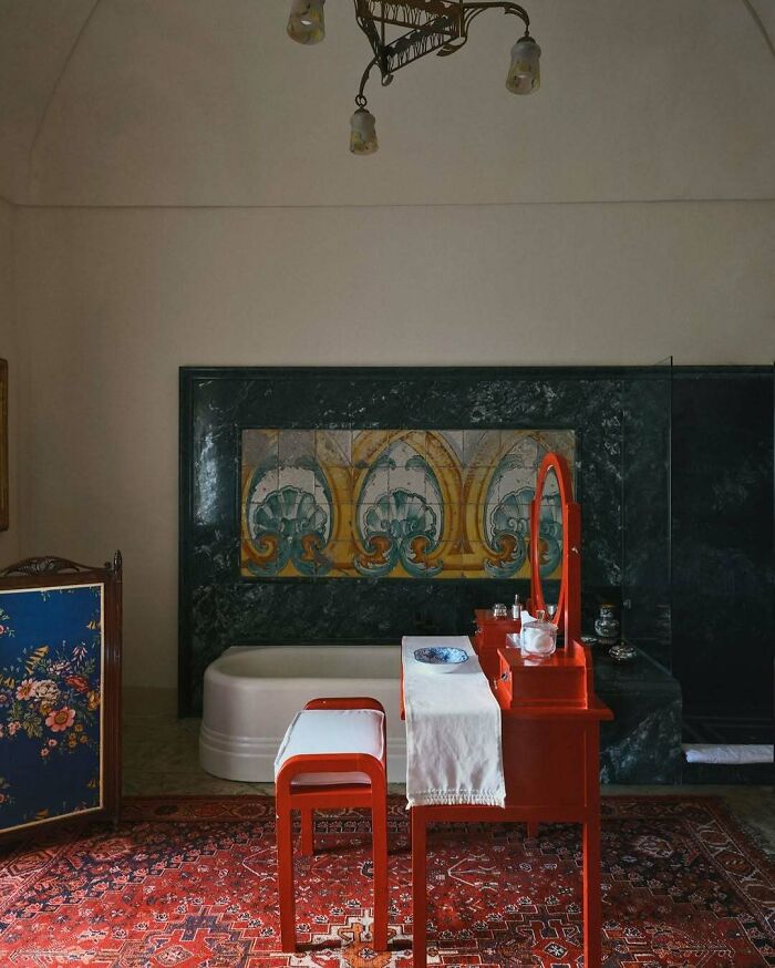 Bold and beautiful interiors featuring vibrant red vanity, detailed artwork, and a richly patterned carpet in a stylish bathroom setting