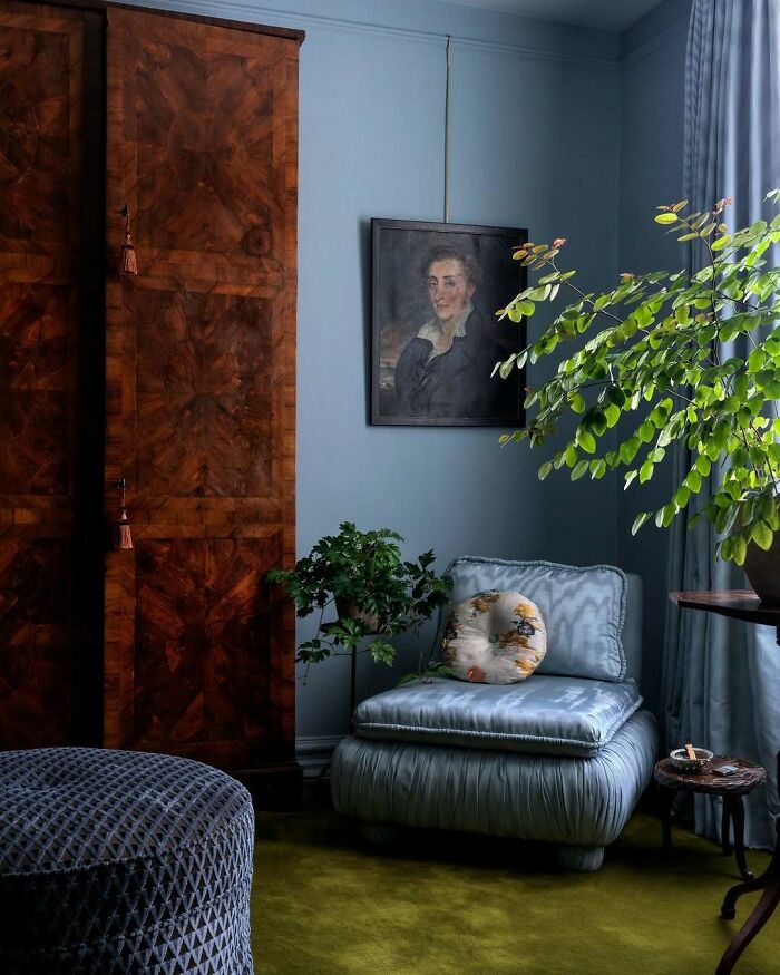 Cozy corner with bold and beautiful interiors featuring a plush blue chair, vintage cabinet, and lush green plants.