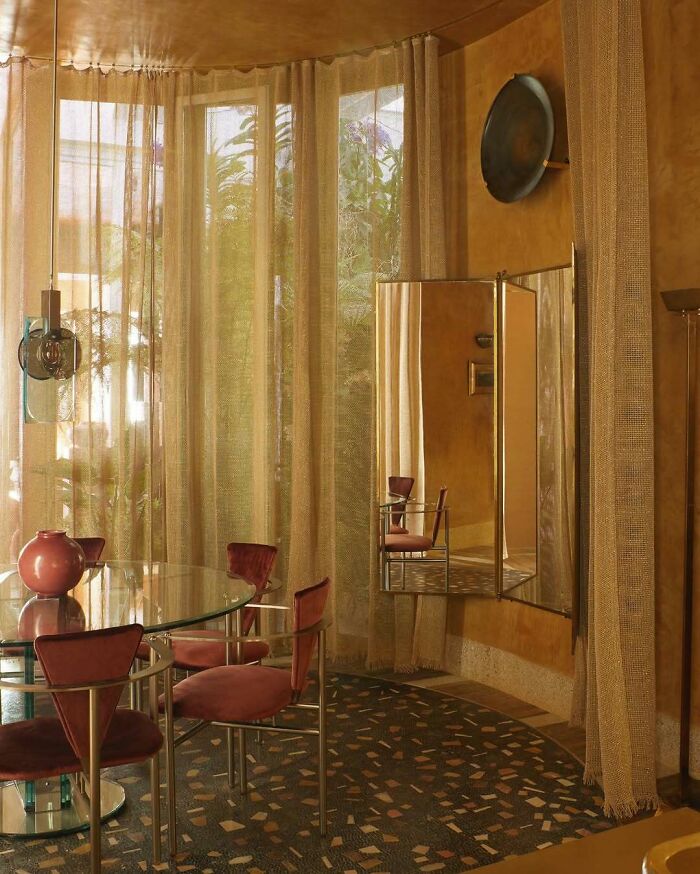 Bold and beautiful interiors featuring a glass dining table, velvet chairs, sheer curtains, and warm earthy tones in a stylish room.