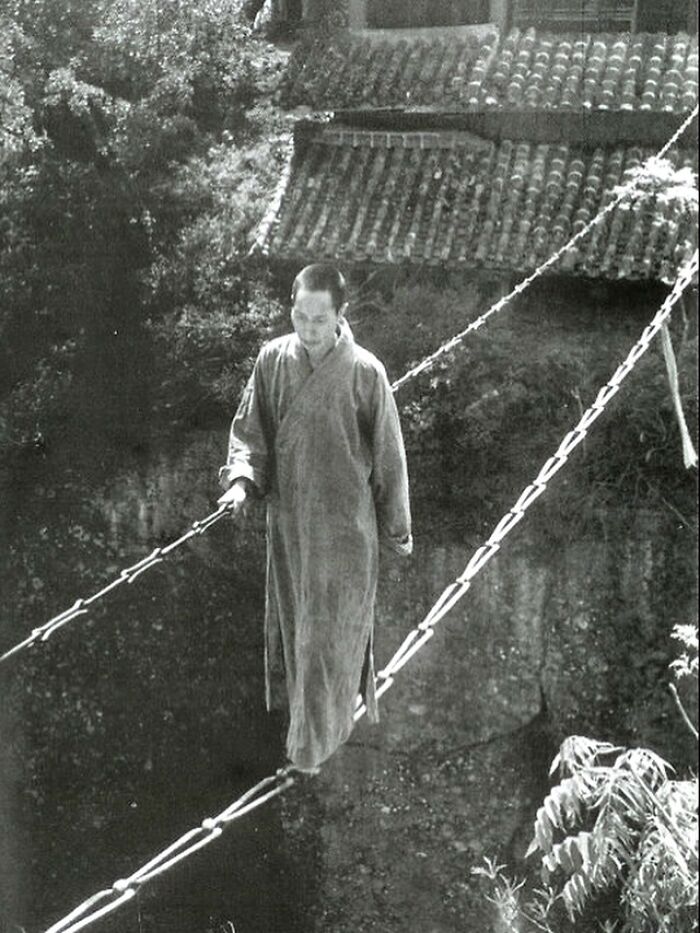 Person carefully crossing a traditional rope bridge, showcasing an amazing architectural structure of human creativity.