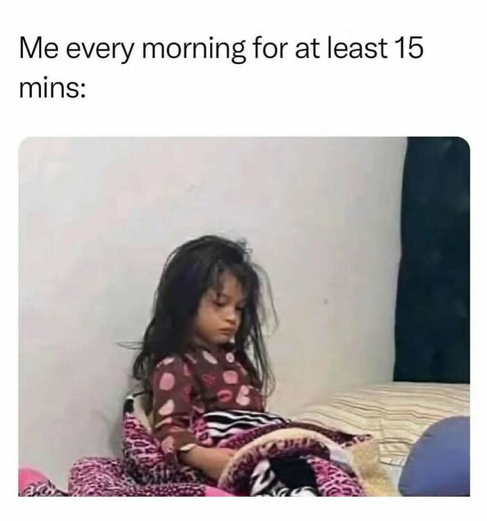 Tired young girl sitting on bed wrapped in blankets, illustrating a cute and wholesome morning moment for girlies.