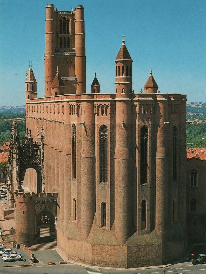 Massive historic brick architectural structure with tall towers and intricate gothic design under clear blue sky.