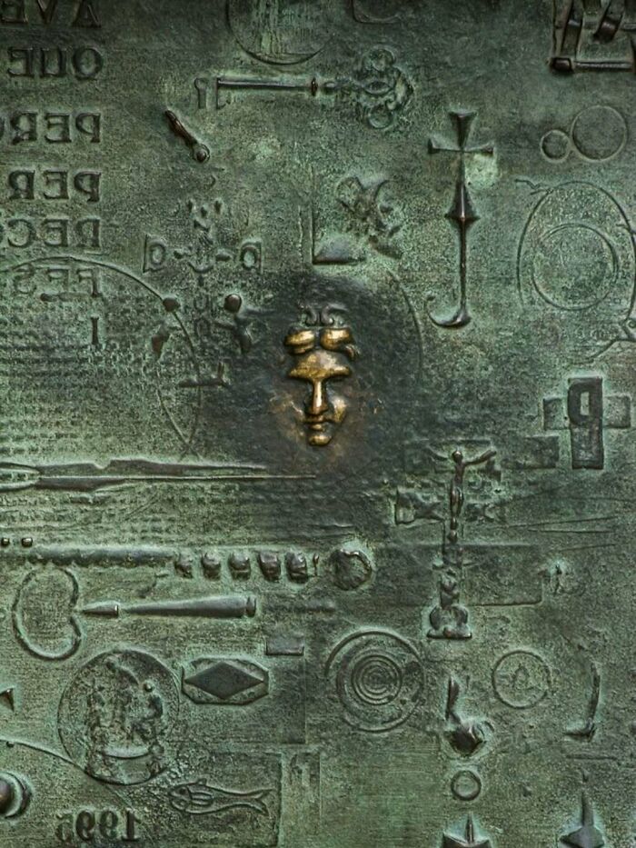 Abstract bronze architectural structure with intricate symbols and a golden face, showcasing creativity in architectural design.