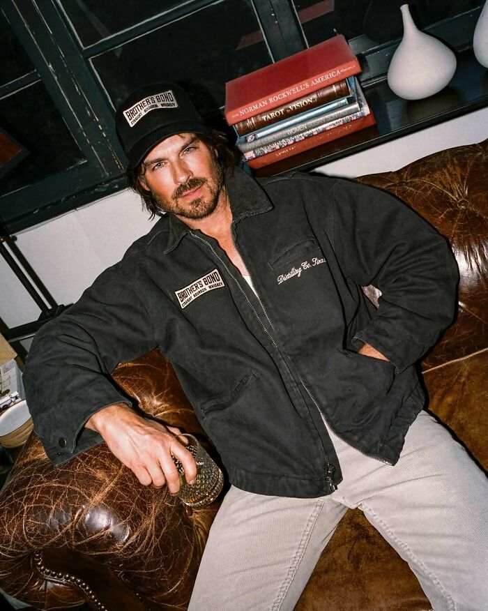 Man wearing a black jacket and cap sitting on a leather couch holding a glass, representing iconic actors who vanished from Hollywood.