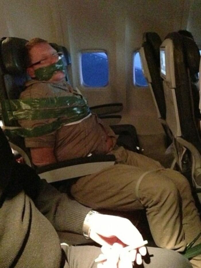 Man taped to airplane seat with green tape in a weirdly hilarious image capturing an unusual travel moment.