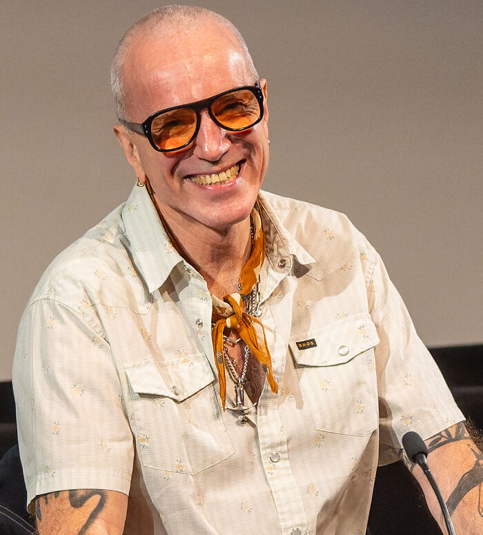 Smiling iconic actor with orange sunglasses and tattoos speaking at a panel, representing actors who dominated Hollywood then vanished.