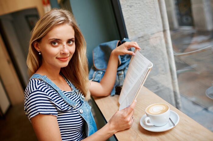 Young woman reading a book and drinking coffee at a cafe, illustrating red flags in dating after the first date.