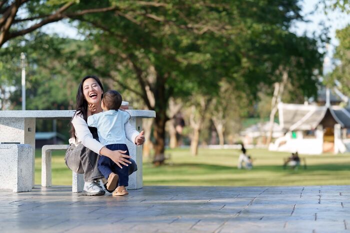 Woman laughing and hugging child outdoors, illustrating red flags that got people running away after the first date.