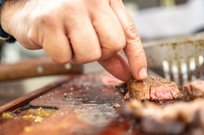 Close-up of hand picking up cooked steak piece on wooden cutting board, highlighting red flags in dating scenarios.