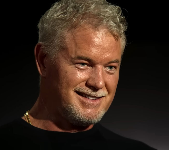 Eric Dane smiling in a close-up portrait with grey hair and beard against a black background