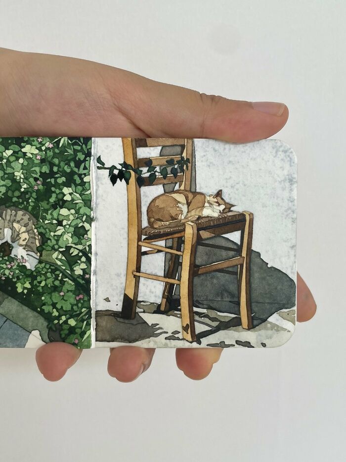 Hand holding a card featuring Gegyjiji’s dreamy watercolor painting of a cat sleeping on a wooden chair outdoors.