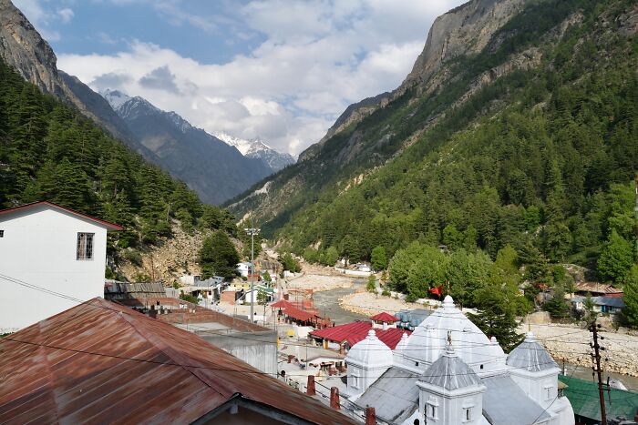 Mountain valley with green forests, river, and white temple rooftops, reflecting spiritual tourism in India.