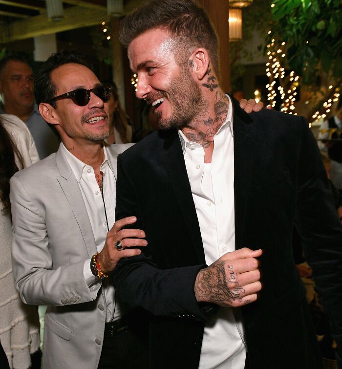 Marc Anthony and Brooklyn Beckham interacting at a social event with warm lighting and festive background decor.