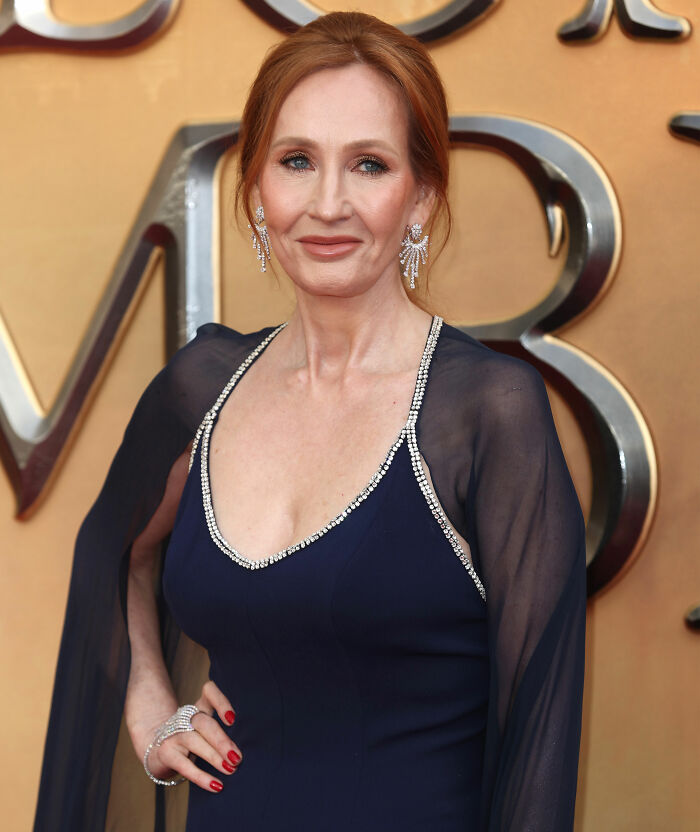 Author in elegant navy dress with jeweled trim and earrings at an event, linked to Harry Potter fans and JK Rowling controversy.