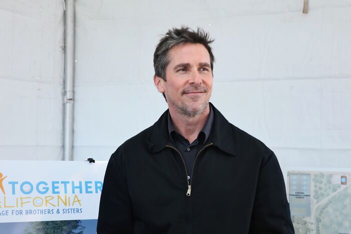 Christian Bale at an event, wearing a black jacket, representing Heat 2 and the DC showdown buzz.