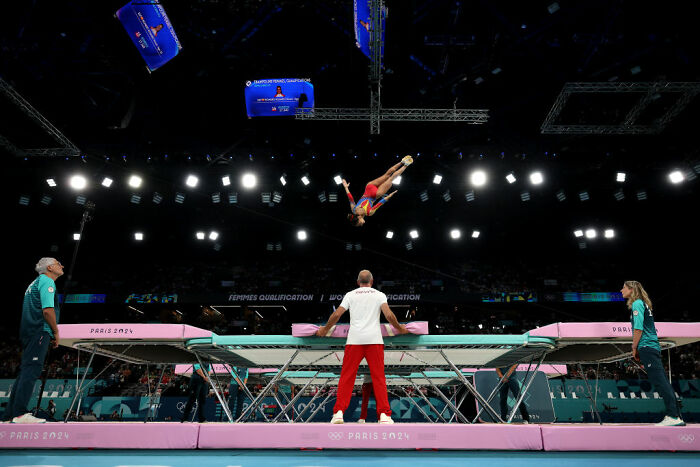 Olympic trampoline athlete mid-flip over the trampoline during a high-intensity Olympic sport competition.