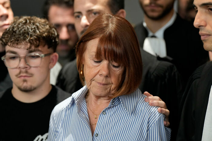 Gisèle Pelicot looking somber surrounded by lawyers and supporters during a legal proceeding about exploitation allegations.