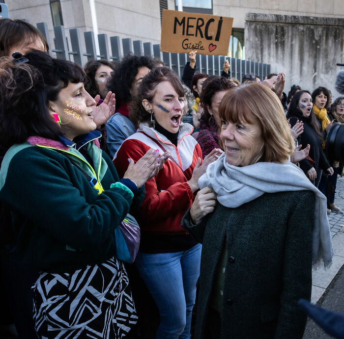 Women cheering outdoors with a Merci sign, showing support related to Gisèle Pelicot and exploitation awareness.