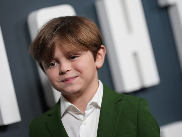 Young boy cast as Atreus in God of War TV show wears green jacket and white shirt, attending a formal event.