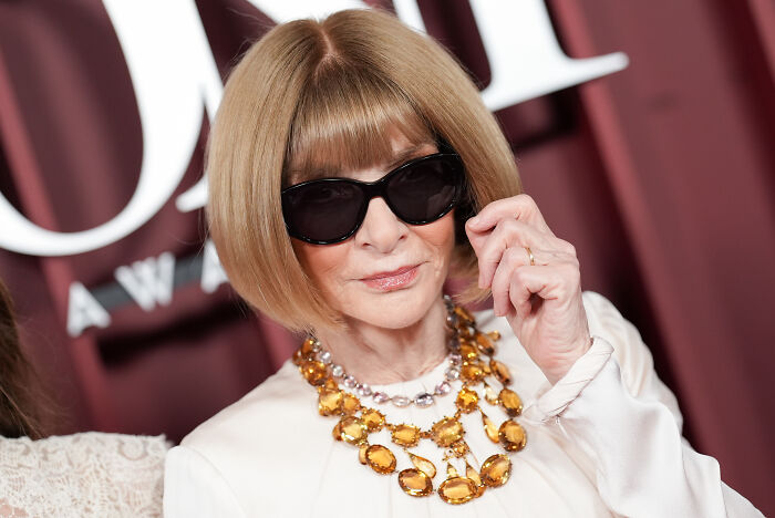 Woman with bob haircut wearing black sunglasses and a statement necklace at a formal event discussing Met Gala dress code controversy.