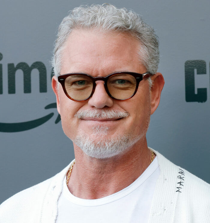 Eric Dane smiling at a public event wearing glasses and a white shirt, capturing fans' hearts before his tragic passing.