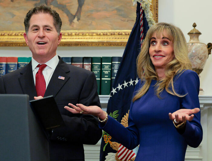 Woman displaying strange behavior during White House press conference standing beside a man in a suit speaking at podium.