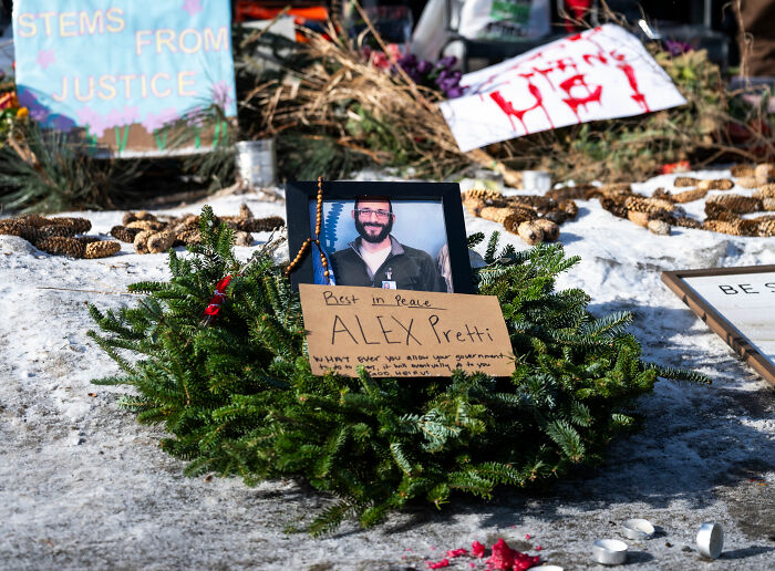 Memorial wreath with photo of Alex Pretti and signs about justice and medical examiner's ruling at snowy outdoor site.