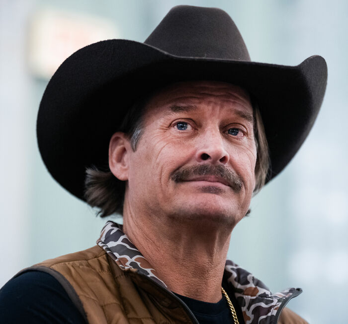 Kid Rock wearing a black cowboy hat and brown vest, looking reflective after alternative halftime show.