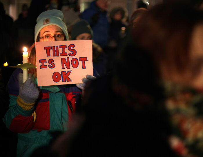 Person holding a candle and a sign at night, reflecting emotions around Alex Pretti's case medical examiner ruling update.