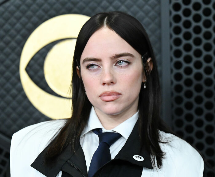 Billie Eilish looking sideways in a black and white outfit at a media event with a CBS logo background.