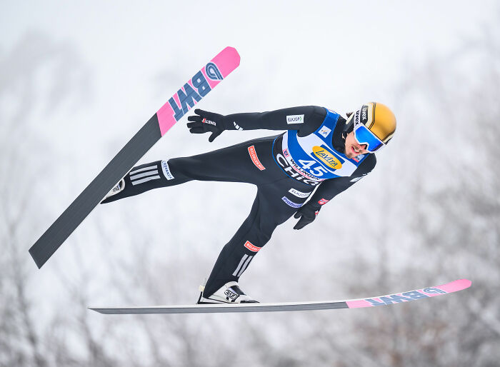 Ski jumper in mid-air during Winter Olympics event, highlighting controversy over manhood scandal and rule change.